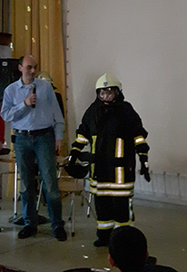 Andreas Höwer erläutert die Bekleidung der Feuerwehr, die spontan ein Jugendlicher angezogen hatte.